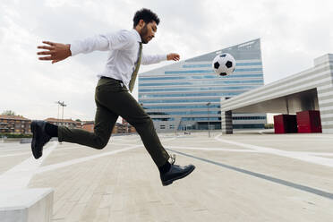 Businessman playing with soccer ball in city - MEUF04164