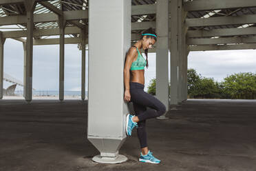 Female athlete looking down while leaning on pillar - MTBF01084