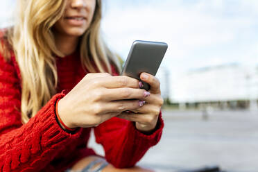 Frau benutzt Smartphone, während sie auf dem Gehweg sitzt - MGOF04737