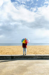 Mid erwachsene Frau stehend mit bunten Regenschirm am Strand - MGOF04750