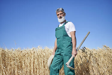 Lächelnder Landwirt mit Hacke auf einem Weizenfeld - KIJF04131