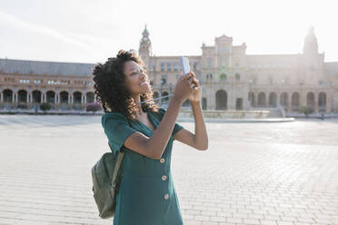 Lächelnde Touristin beim Fotografieren mit dem Smartphone auf der Plaza De Espana, Sevilla, Spanien - JRVF01507