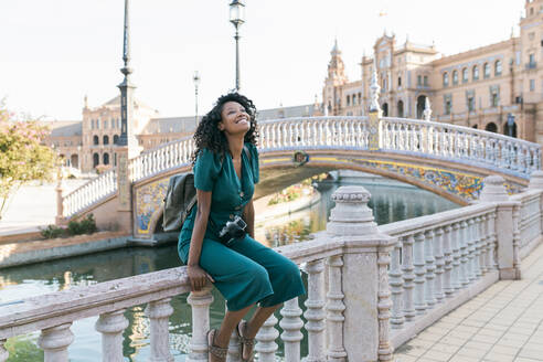 Glückliche Afro-Frau, die auf dem Geländer der Plaza De Espana, Sevilla, Spanien, sitzt - JRVF01520