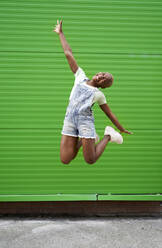 Aufgeregte Frau, die vor eine grüne Wand springt - VEGF04870