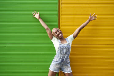 Fröhliche junge Frau mit erhobenen Armen vor einer zweifarbigen Wand - VEGF04895