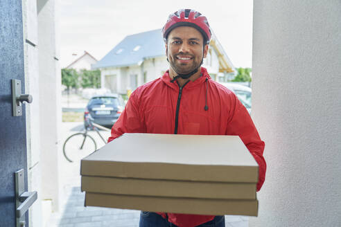 Männlicher Pizzalieferant, der einen Pizzakarton hält und an der Tür steht - ABIF01453