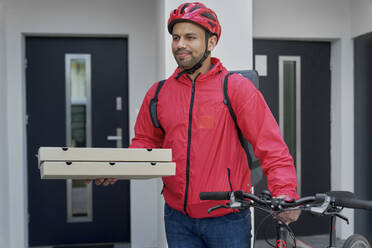 Pizzabote mit Pizzakartons und Fahrrad vor der Haustür stehend - ABIF01457