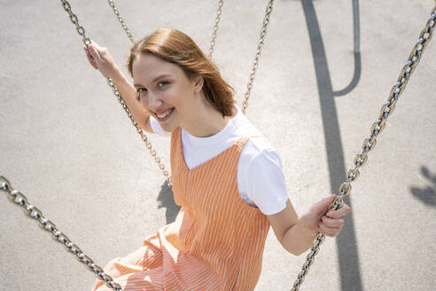 Young woman sitting on swing during sunny day - VPIF04563