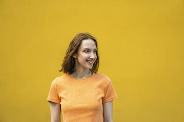 Smiling young woman standing in front of yellow wall - VPIF04607