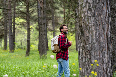 Lächelnder reifer Mann mit Rucksack, der im grünen Wald spazieren geht - SIPF02331