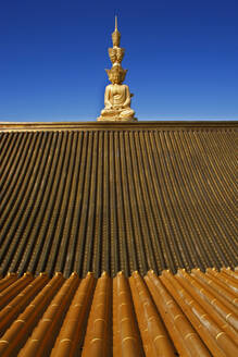 China, Sichuan, Emeishan City, Tiled roof of Buddhist temple at summit of Mount Emei with golden statue of Samantabhadra in background - EAF00060