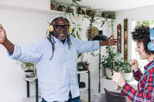 Carefree man listening music through headphones while dancing with daughter at home - ASGF01189