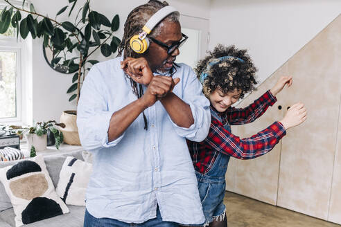 Vater und Tochter mit Kopfhörern tanzen zusammen zu Hause - ASGF01193