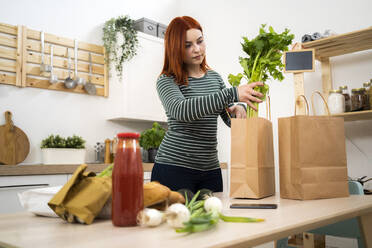 Frau entnimmt Gemüse aus Papiertüten auf dem Tisch - GIOF13206