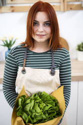 Woman with apron holding leaf vegetable in kitchen - GIOF13216