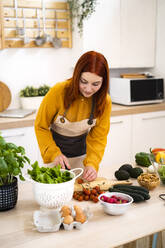 Frau bereitet Essen zu, während sie am Tisch steht - GIOF13225