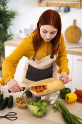 Woman with cutting board preparing food at table in kitchen - GIOF13227