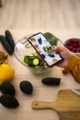 Woman taking photo of vegetables through smart phone at table - GIOF13230