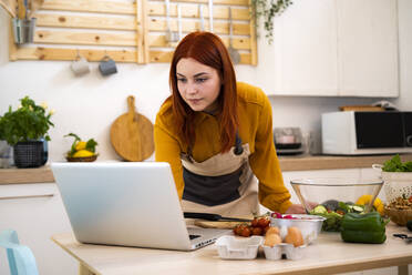 Woman using laptop while preparing salad at kitchen - GIOF13233