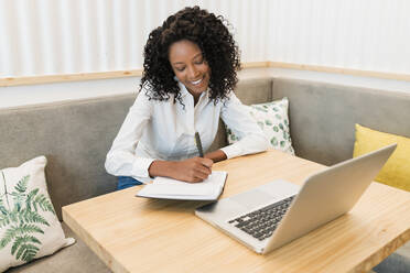 Lächelnde Geschäftsfrau schreibt in ein Buch, während sie in einem Café sitzt - JRVF01556