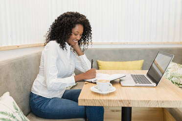 Female freelancer writing in book while sitting at cafe - JRVF01557