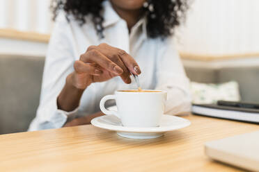 Geschäftsfrau rührt mit Löffel in Kaffeetasse im Café - JRVF01558