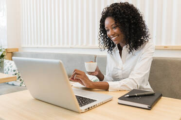 Businesswoman with coffee cup smiling at video call through laptop in cafe - JRVF01560