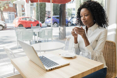 Businesswoman with coffee cup listening to video call through laptop at cafe - JRVF01561