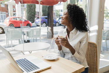 Smiling businesswoman holding coffee cup while looking through cafe window - JRVF01562