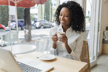 Lächelnde Geschäftsfrau mit Kaffeetasse in der Hand und Blick auf den Laptop - JRVF01563