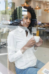 Thoughtful businesswoman with coffee cup looking through cafe window - JRVF01567
