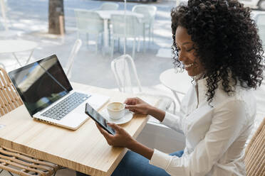 Freiberuflerin, die im Café sitzend ein Mobiltelefon benutzt - JRVF01571