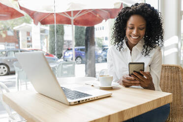 Lächelnde Geschäftsfrau, die ein Mobiltelefon benutzt, während sie in einem Café sitzt - JRVF01572