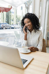 Lächelnde Geschäftsfrau, die in einem Café mit ihrem Handy telefoniert - JRVF01573