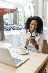 Lächelnde Freiberuflerin, die in einem Café sitzt und ihr Handy benutzt - JRVF01574