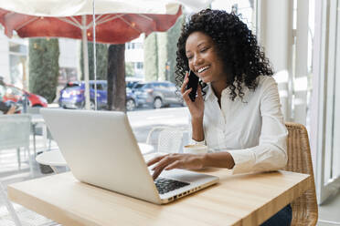 Geschäftsfrau, die mit dem Handy telefoniert und einen Laptop in einem Café benutzt - JRVF01575