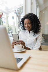 Female freelancer using mobile phone while sitting at cafe - JRVF01578