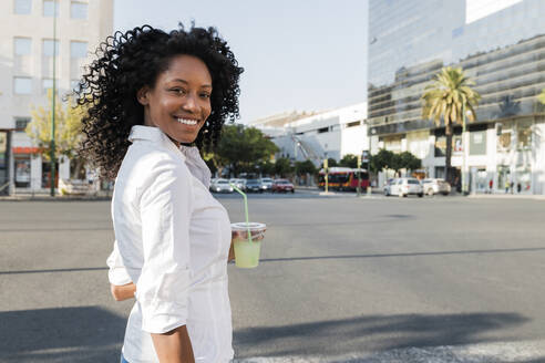 Smiling businesswoman holding drink while standing at city street - JRVF01586