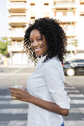 Lächelnde Geschäftsfrau mit Saft in der Hand auf der Straße stehend - JRVF01588