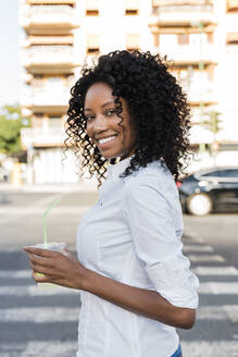 Smiling businesswoman holding juice while standing on road - JRVF01588