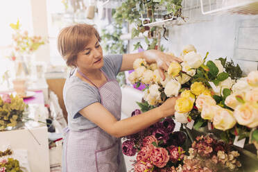 Ältere Blumenladenbesitzerin arrangiert Blumen im Laden - LJF02278