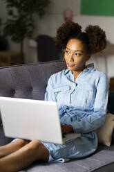 Junge Frau, die mit einem Laptop auf dem Sofa sitzt und im Wohnzimmer nachdenkt - GIOF13241