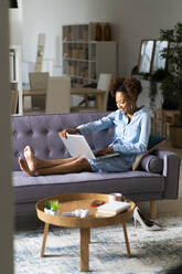 Lächelnde junge Frau mit Laptop auf dem Sofa im Wohnzimmer zu Hause - GIOF13245