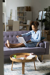 Smiling young woman using laptop on sofa in living room at home - GIOF13245