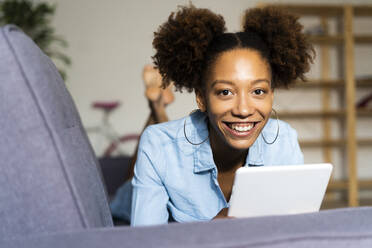 Lächelnde Frau mit digitalem Tablet auf dem Sofa im Wohnzimmer liegend - GIOF13260