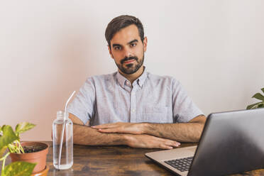 Mann sitzt mit Laptop und Wasserflasche am Schreibtisch - MGRF00373