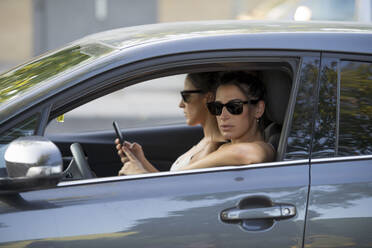 Frau schaut durch das Fenster, während Zwillingsschwester im Auto ihr Smartphone benutzt - OCMF02210