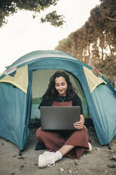 Young woman working on laptop in tent during weekend - GRCF00854