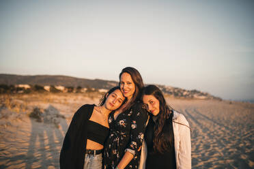 Smiling daughters leaning on shoulder of mother at beach - GRCF00857
