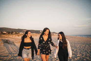 Smiling mother and daughters walking at beach during sunset - GRCF00858